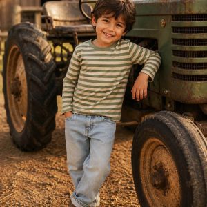 boy leaning against an old tractor wearing a kids on trend striped tshirt and blue jeans