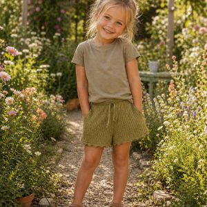 little girl in some kids on trend lacey green shorts and a green top standing in a garden
