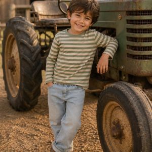 boy leaning against an old tractor wearing a kids on trend green t-shirt and blue jeans