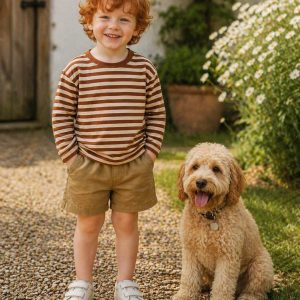 a boy standing beside a puppy and wearing a kids on trend striped brown tshirt and fawn shorts