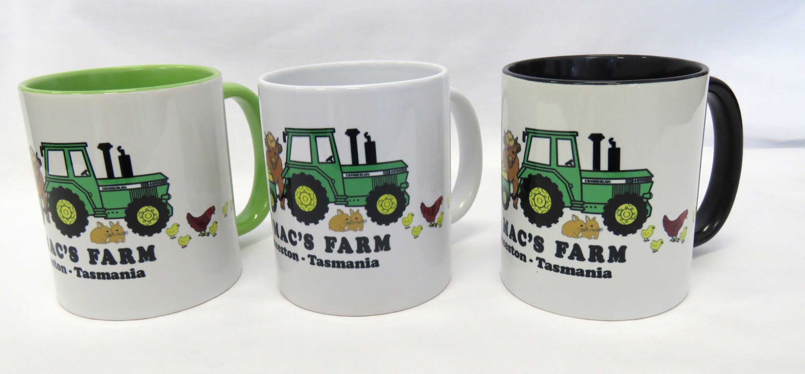 three old macs coffee mugs in green, white and black with cartoon style green tractor and animals