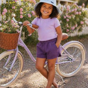 girl wearing purpled shorts and a lilac top standing beside a bicycle