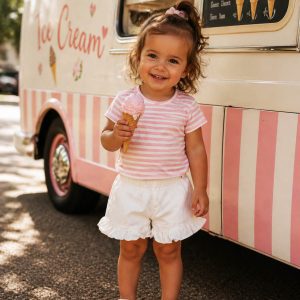toddler wearing kids on trend white frilly shorts and a pink striped tshirt beside an ice cream van